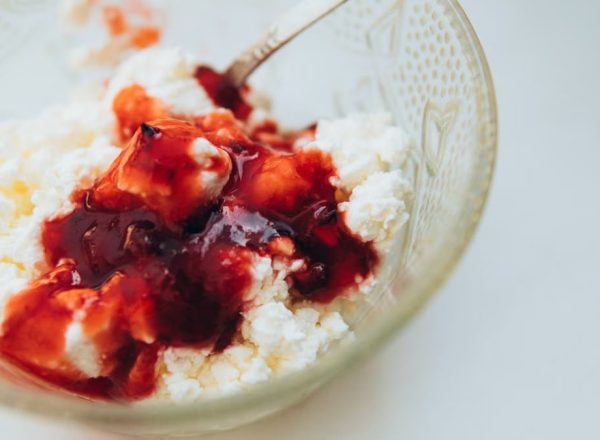 From above of appetizing cottage cheese with berry jam served in glass bowl with spoon on white table