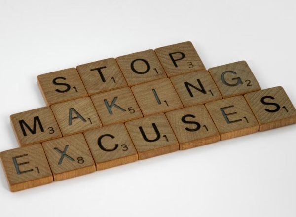 Wooden Scrabble tiles spell 'Stop making excuses' on a white background, encouraging self-improvement.