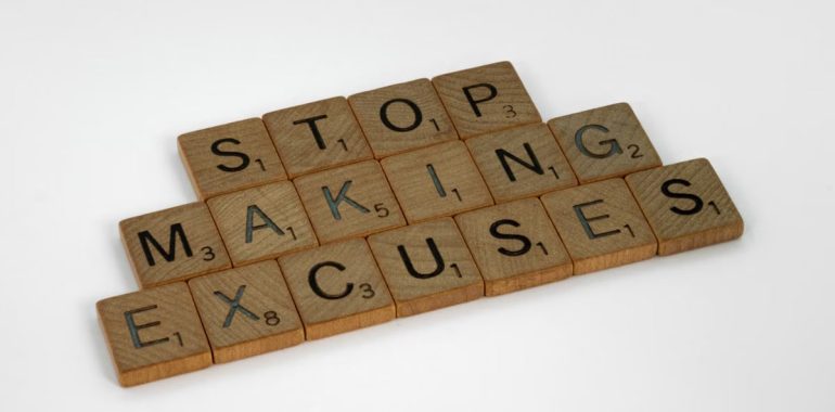 Wooden Scrabble tiles spell 'Stop making excuses' on a white background, encouraging self-improvement.